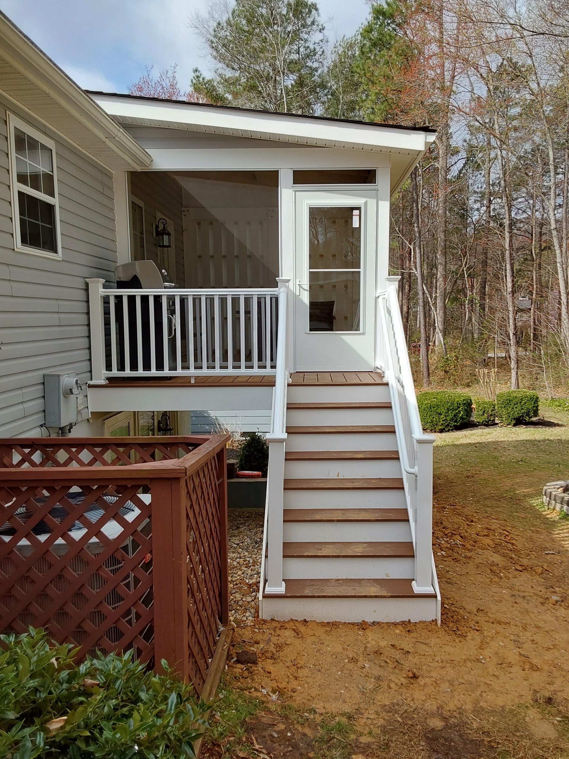 A screened-in porch with steps and a white railing; located outside a house with trees in the background.