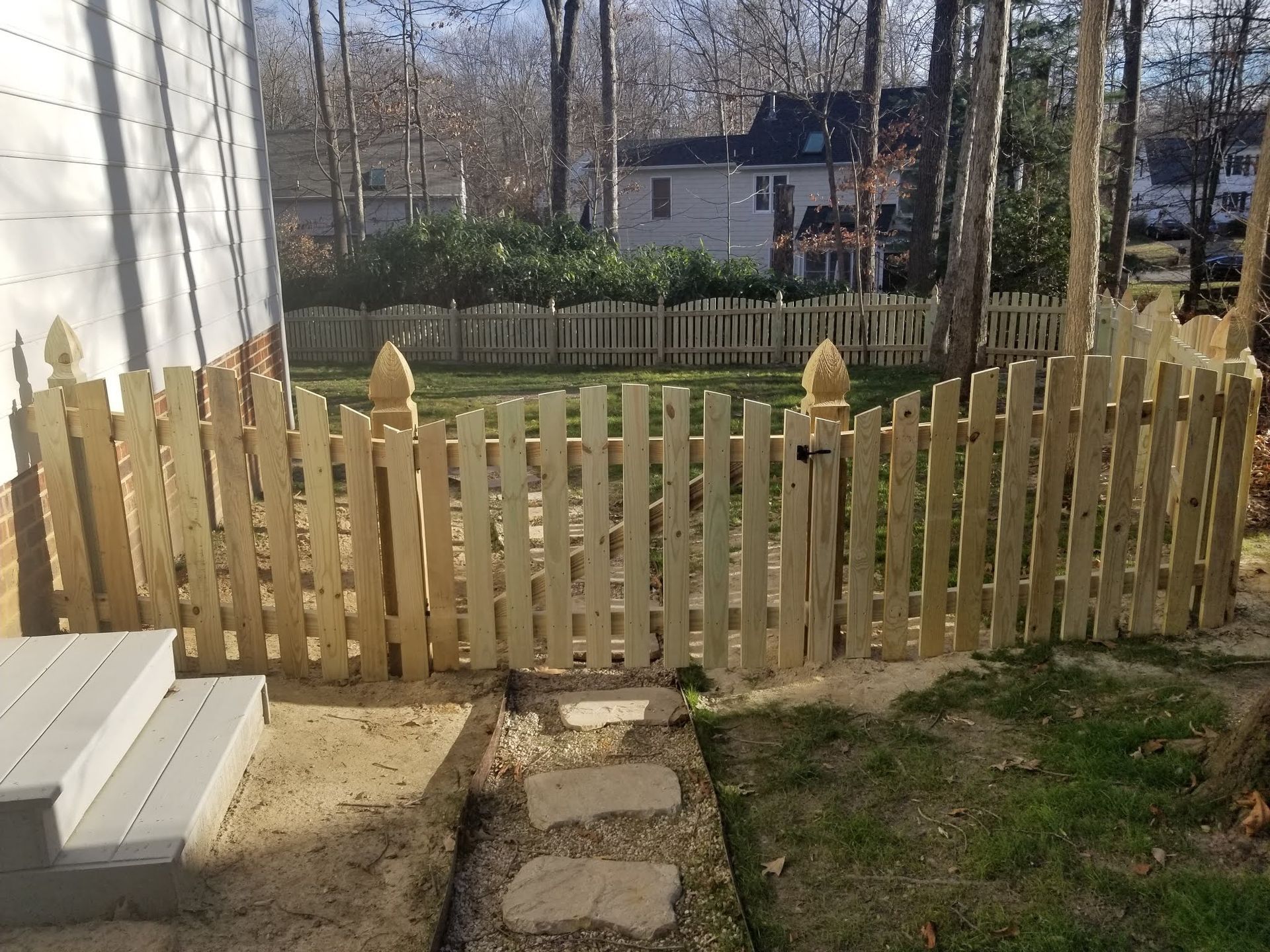 Wooden picket fence with gate, backyard setting.
