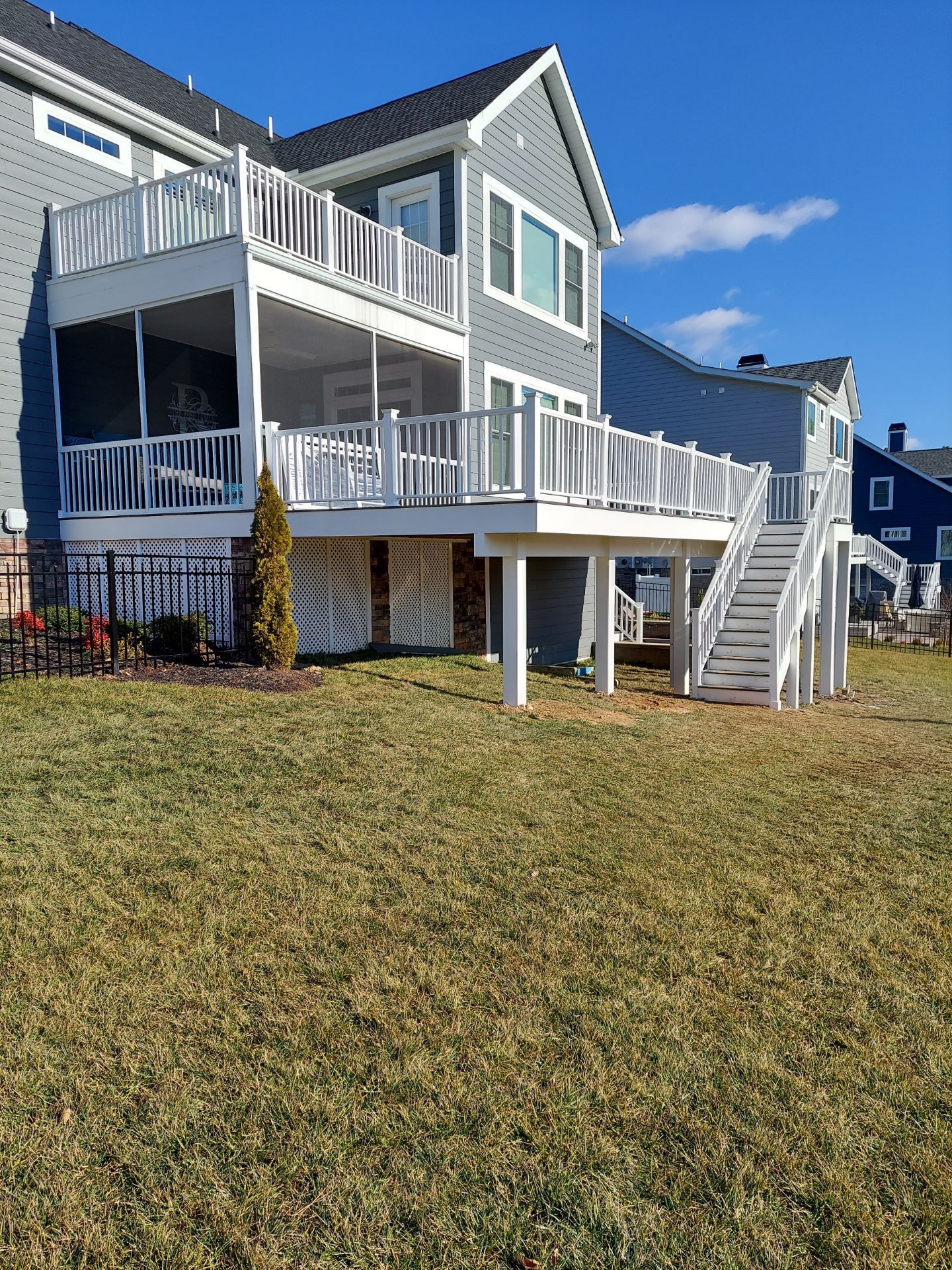 Two-story gray house with white decks and stairs. Overlooking a grassy yard under a blue sky.