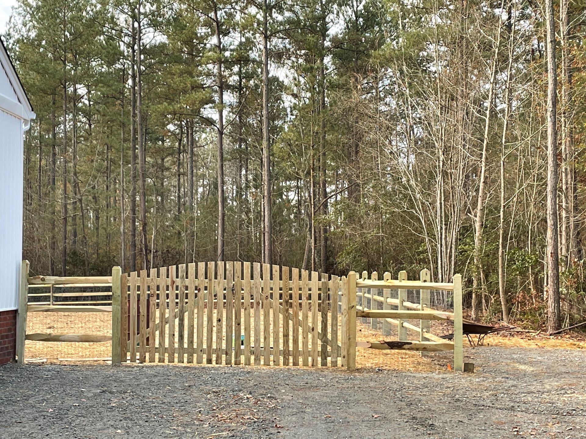 Wooden gate and fence leading into a wooded area. Gravel driveway in foreground.