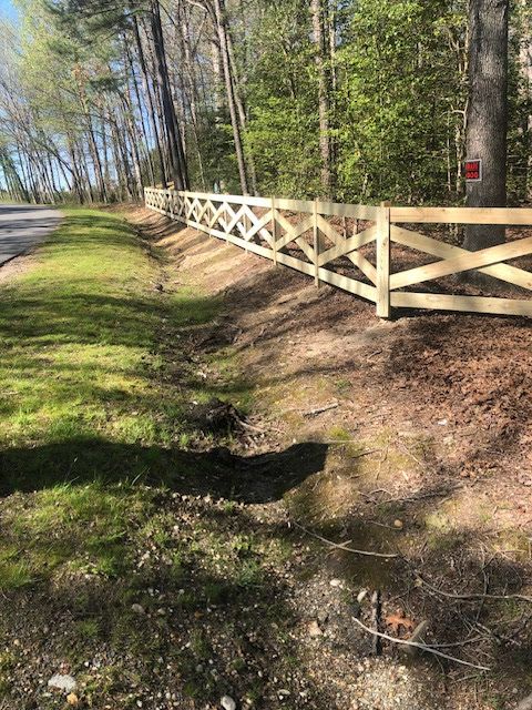 Wooden fence with crisscross design bordering a grassy area next to a road.