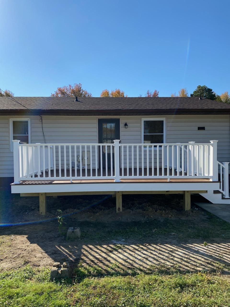 A newly built deck with white railings and brown decking, attached to a house with a blue sky background.