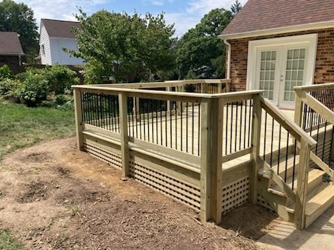 Wooden deck with black railings and steps leading to a brick house.