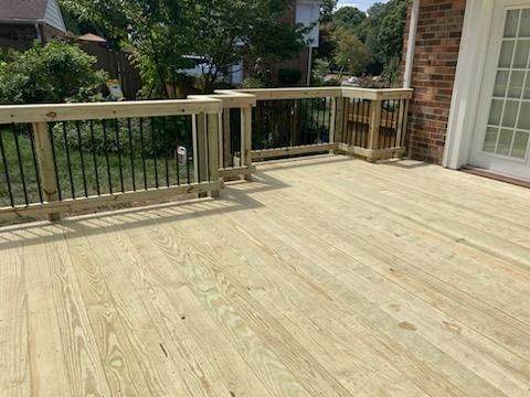 Wooden deck with black railing next to a brick house.