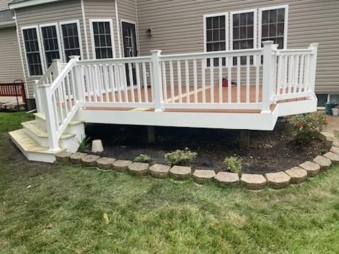 White deck with railings and stairs, brown flooring, overlooking a green lawn with a small garden bed.