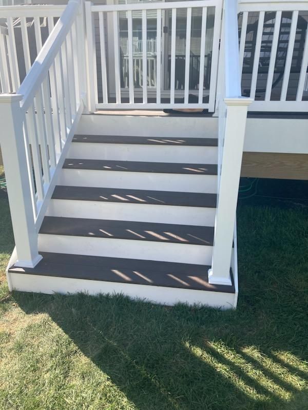 White deck stairs with brown steps leading to a deck with white railings. Green grass surrounds the base.