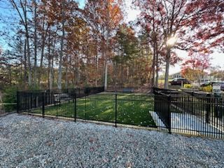 Black fenced dog park with green grass, surrounded by trees and gravel.