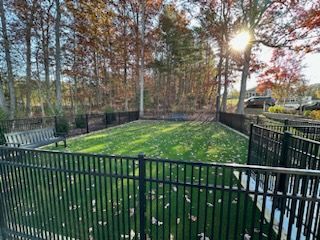 Fenced dog park with green grass, black metal fence, a bench, and trees in the background.