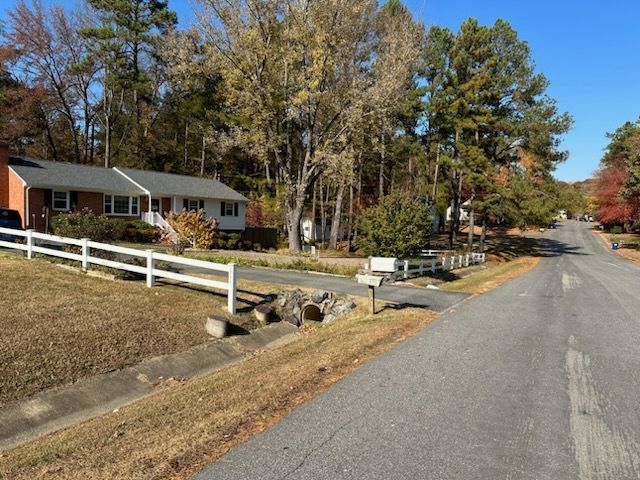 A suburban street with houses, a white fence, and fall foliage; sunny day.