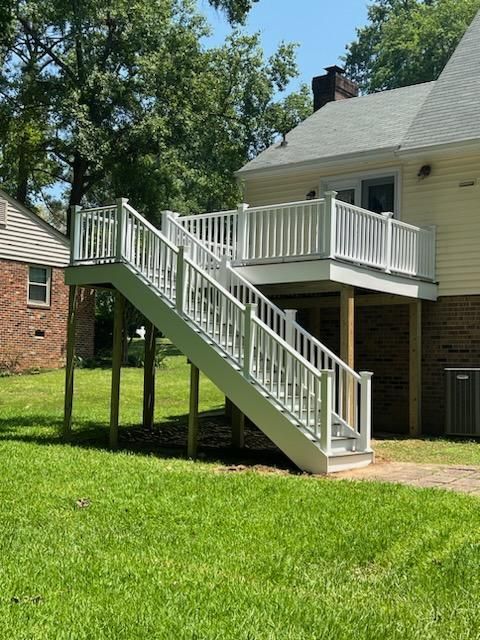 White deck with stairs leading down to a green lawn; backyard setting.