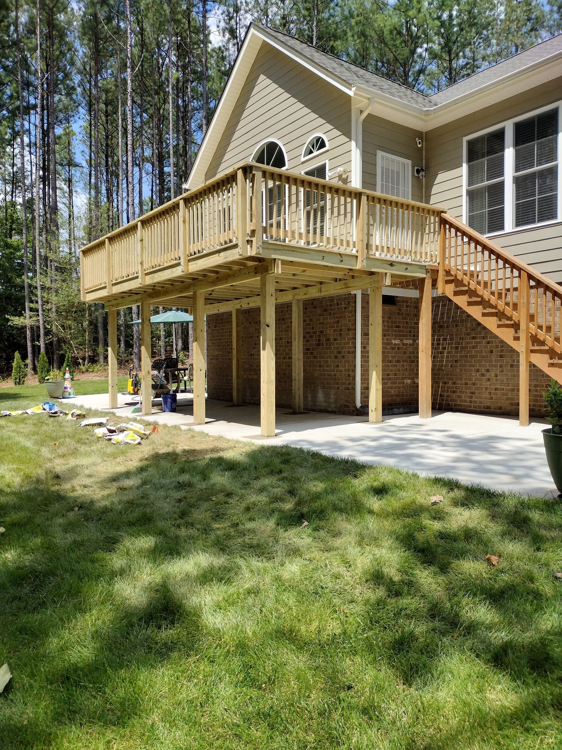 Wooden deck attached to a house with a brick base, stairs, and a concrete patio.