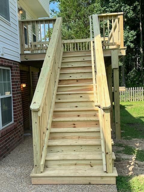 Wooden staircase leading to a raised deck attached to a house; backyard setting.