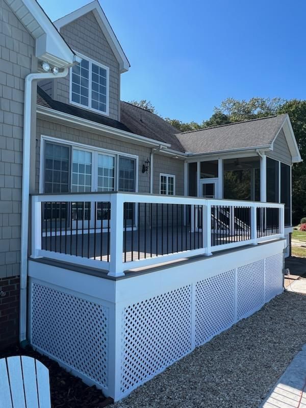 Deck with white lattice skirting and black railings, attached to a house with a screened porch.