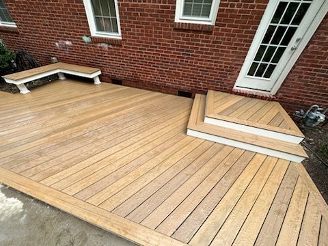 Wooden deck with steps, a bench, and a door, against a red brick building.