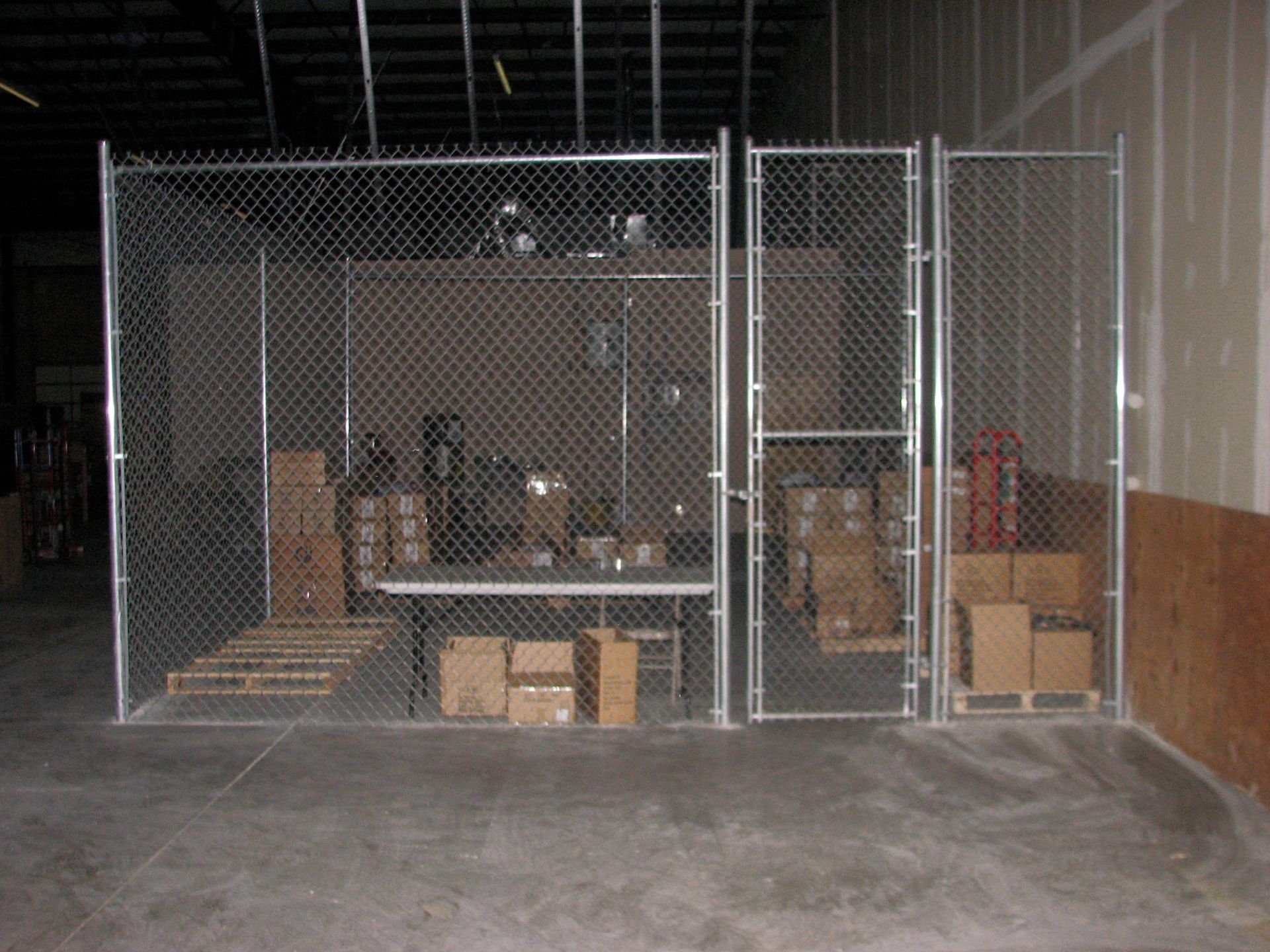Chain-link fence encloses a warehouse storage area with boxes and pallets.