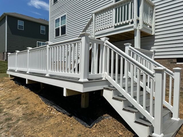 White deck with stairs, against a gray house, on a sunny day.