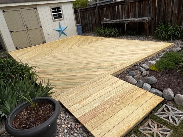 Wooden deck with a square walkway, surrounded by a garden and a shed.