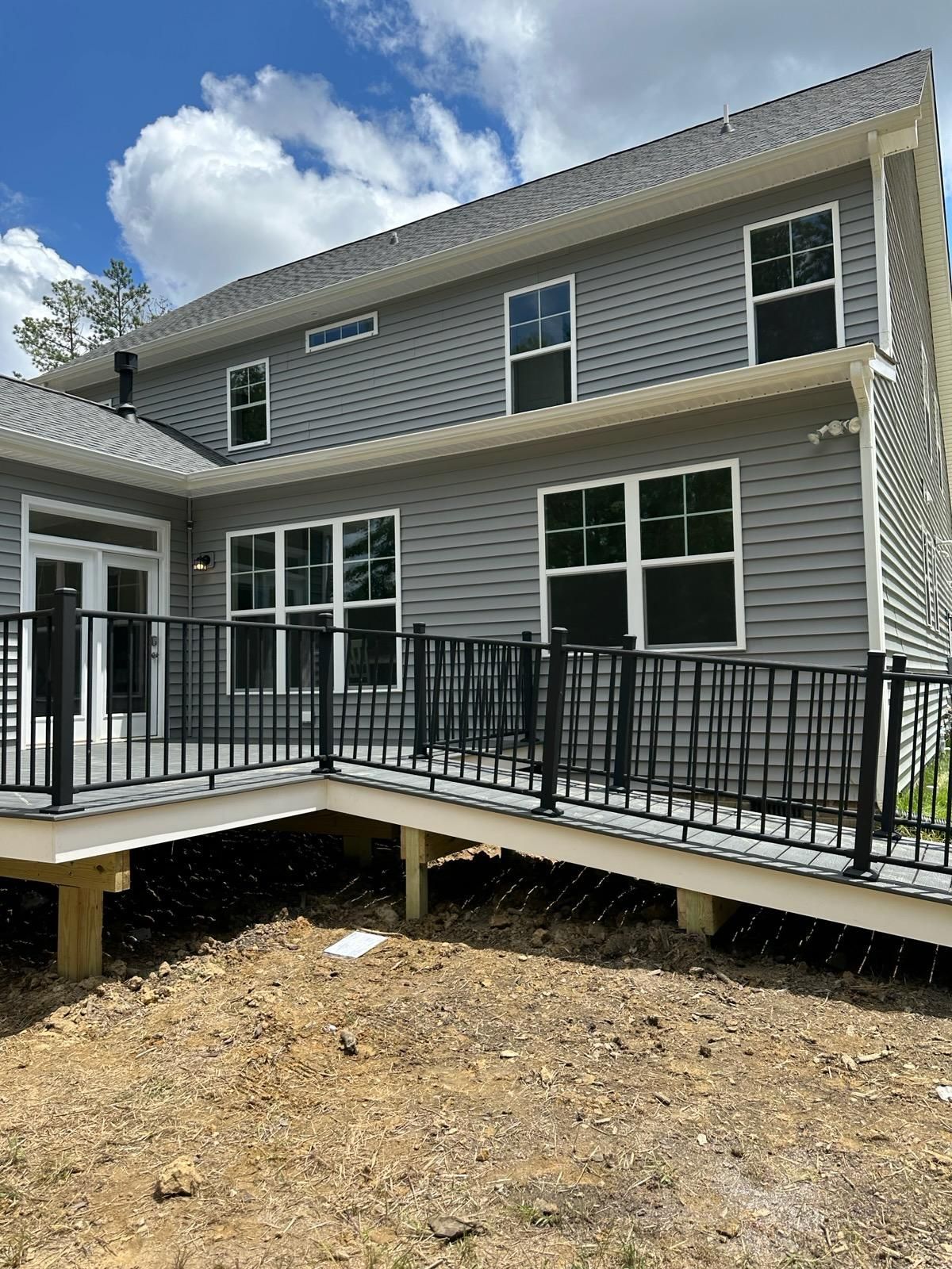 Gray house with black railing deck and ramp. Sunny day with blue sky and clouds.