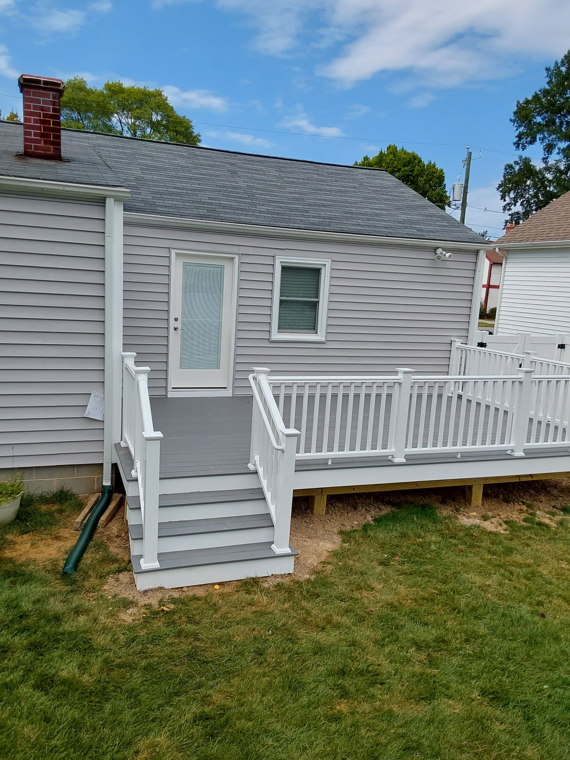 Backyard deck and door of a house painted gray and white, with green grass and a blue sky.