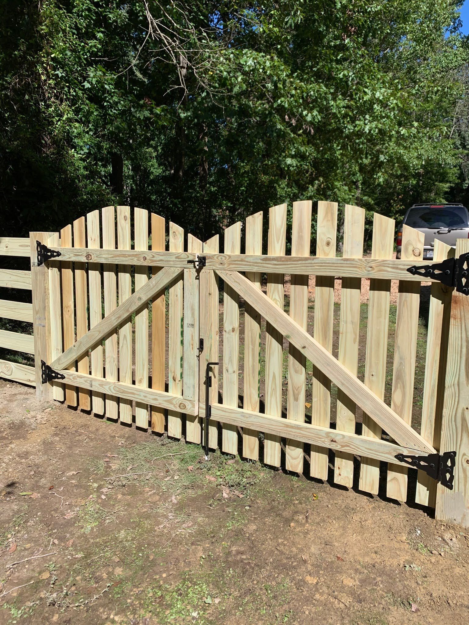 Wooden gate in a backyard, flanked by a wooden fence, with a vehicle visible in the background.
