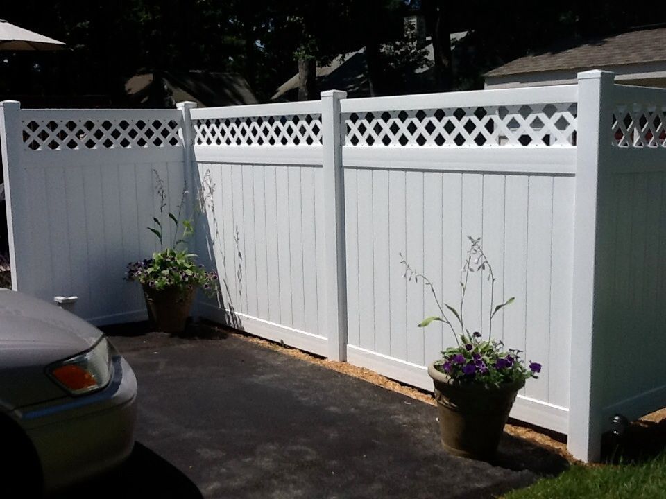 White vinyl fence with lattice top and potted flowers alongside a paved driveway.