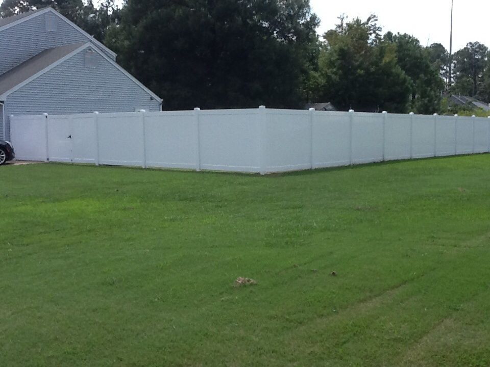White privacy fence surrounding a green lawn, next to a house.