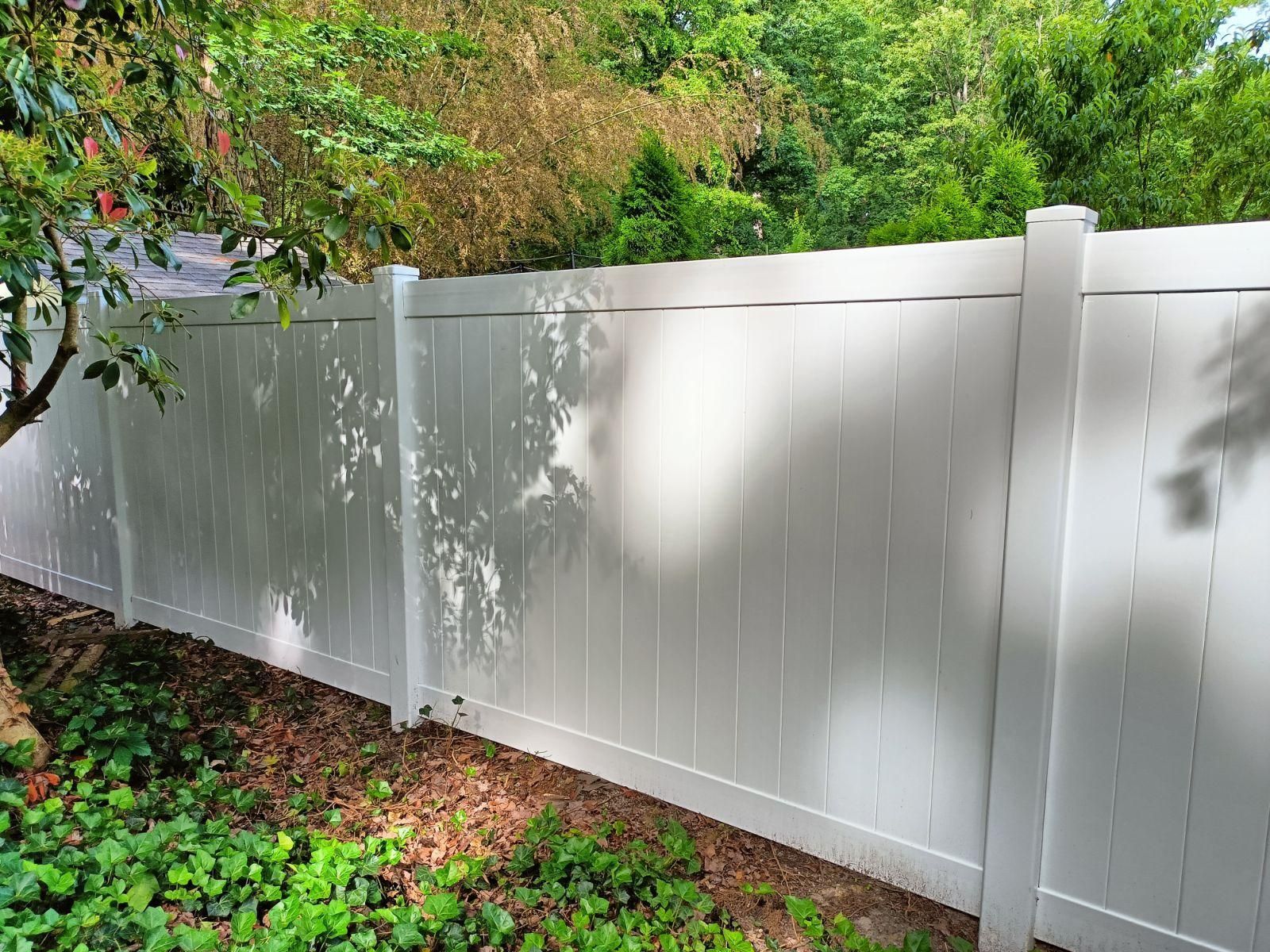 White vinyl fence in a backyard with green foliage.