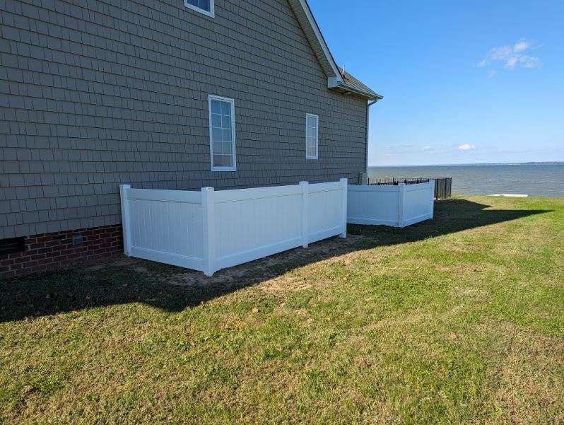 White fenced enclosures next to a house on grassy lawn, with water in the background on a sunny day.