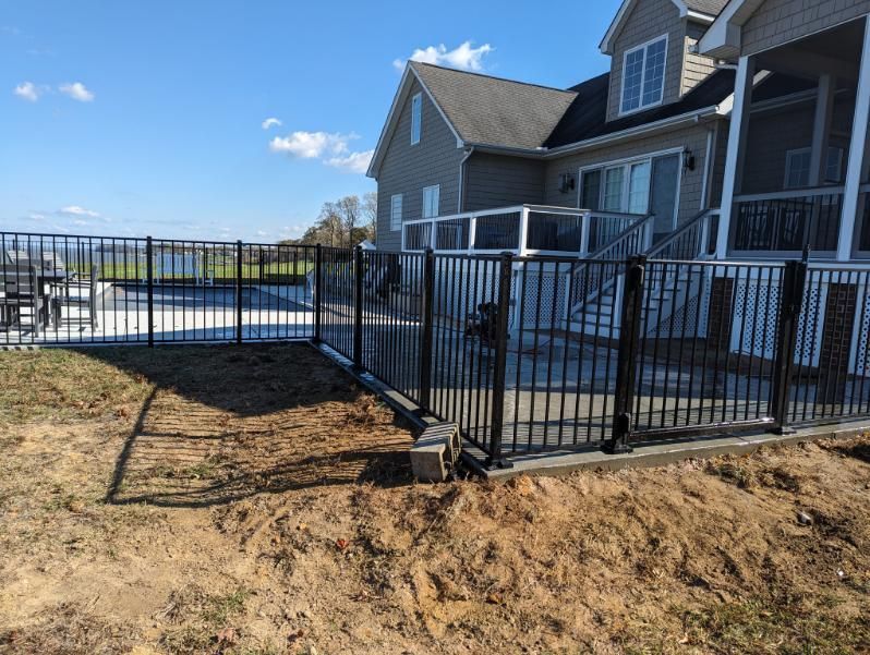 Black metal fence encloses a backyard with a pool and deck, sunny day.