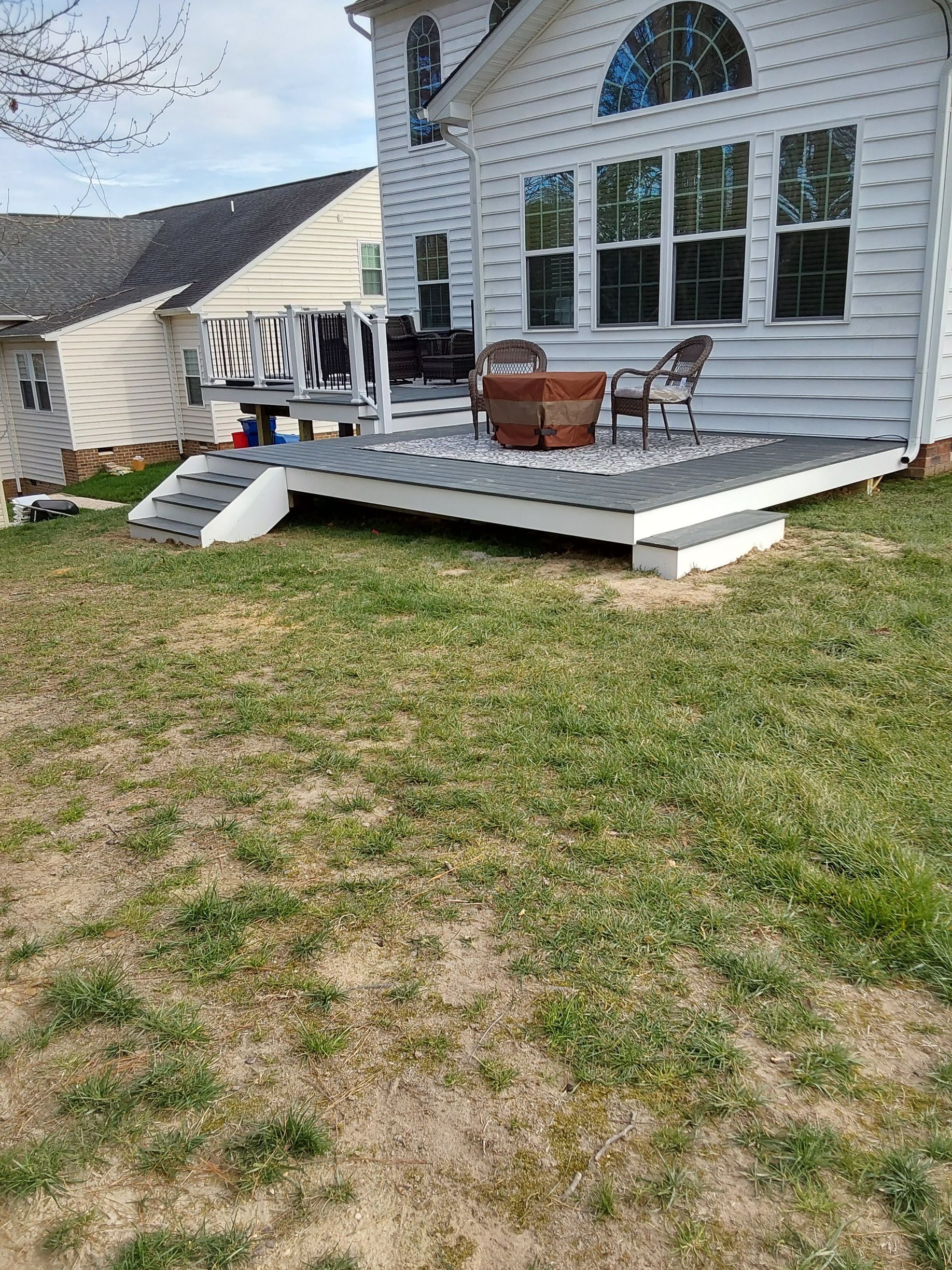 White house with deck and ramp. Gray deck with seating. Green grass in yard.
