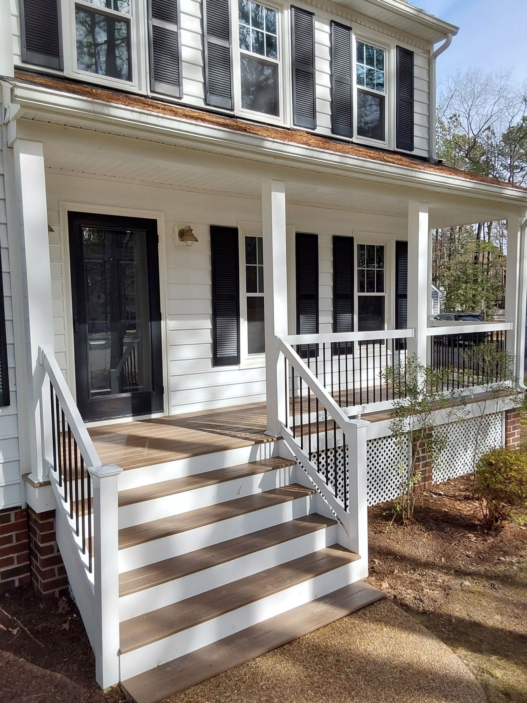 White house with black shutters and door, small porch with steps, sunny outdoor setting.