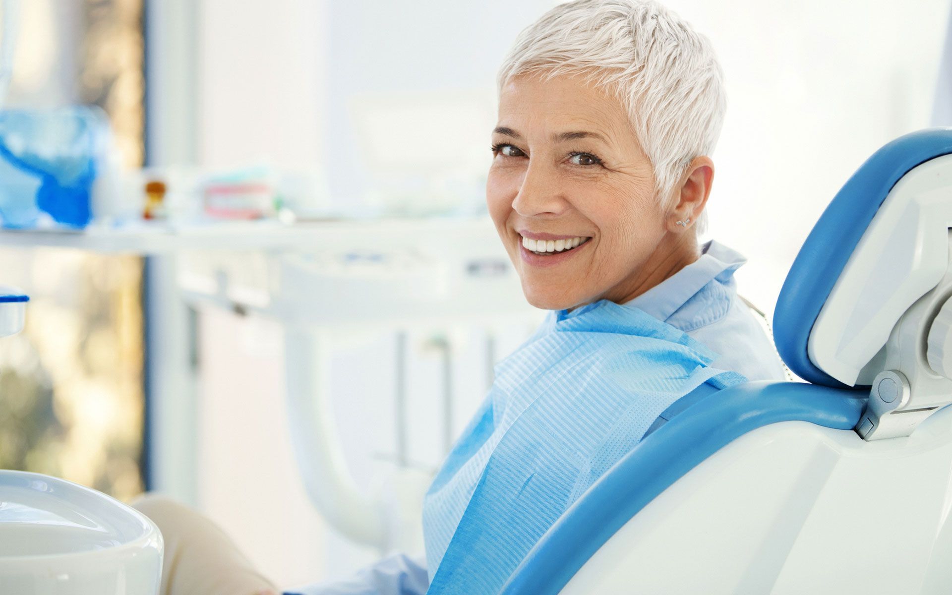 A woman is smiling while sitting in a dental chair.