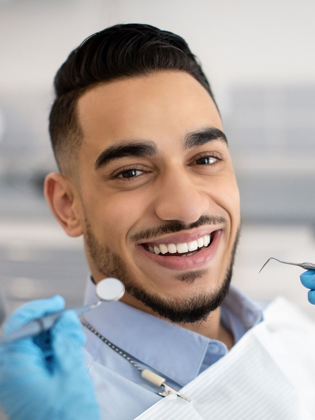 A man is smiling while having his teeth examined by a dentist.