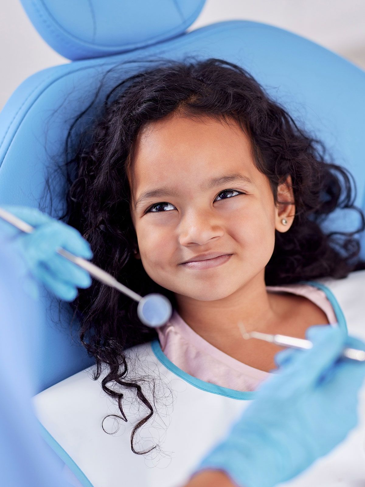 A little girl is sitting in a dental chair while a dentist examines her teeth.
