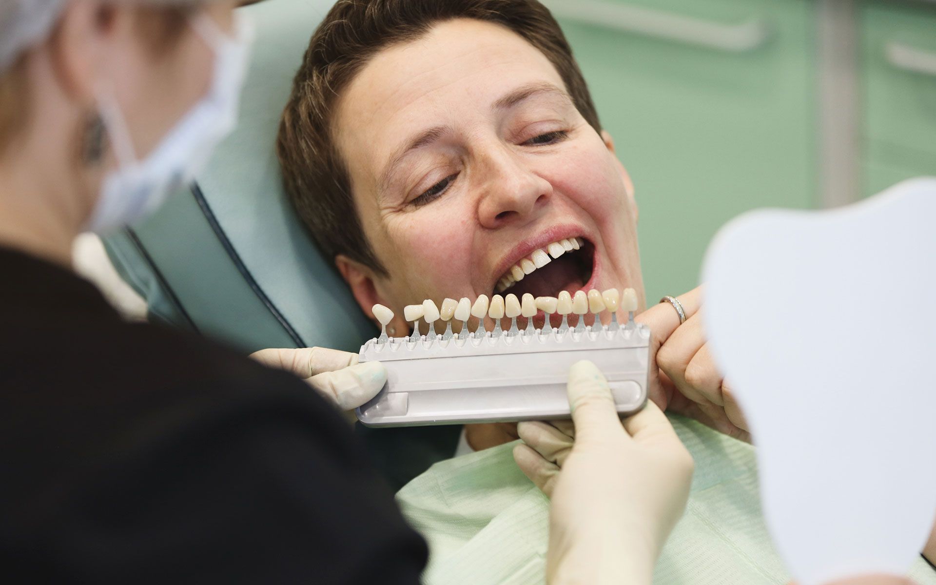 A woman is sitting in a dental chair while a dentist examines her teeth.