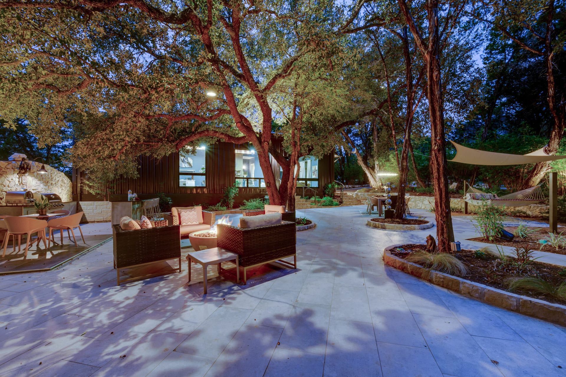 A patio with a lot of furniture and trees in front of a house at night.