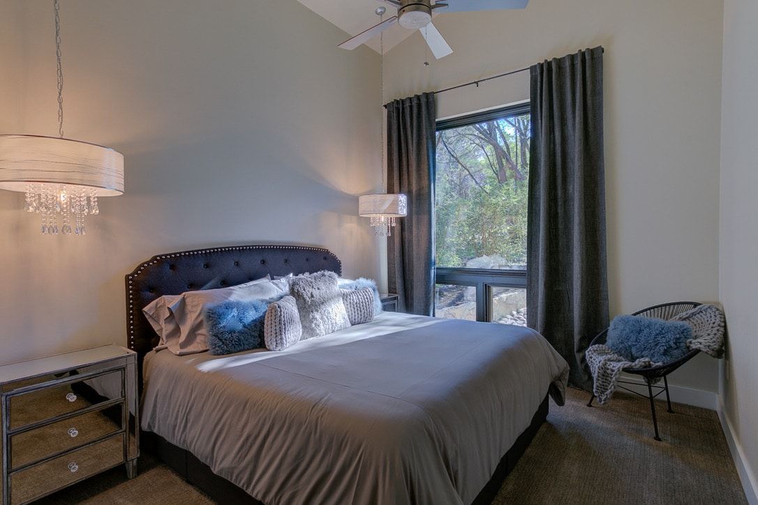 A bedroom with a king size bed , chair , nightstand and ceiling fan.