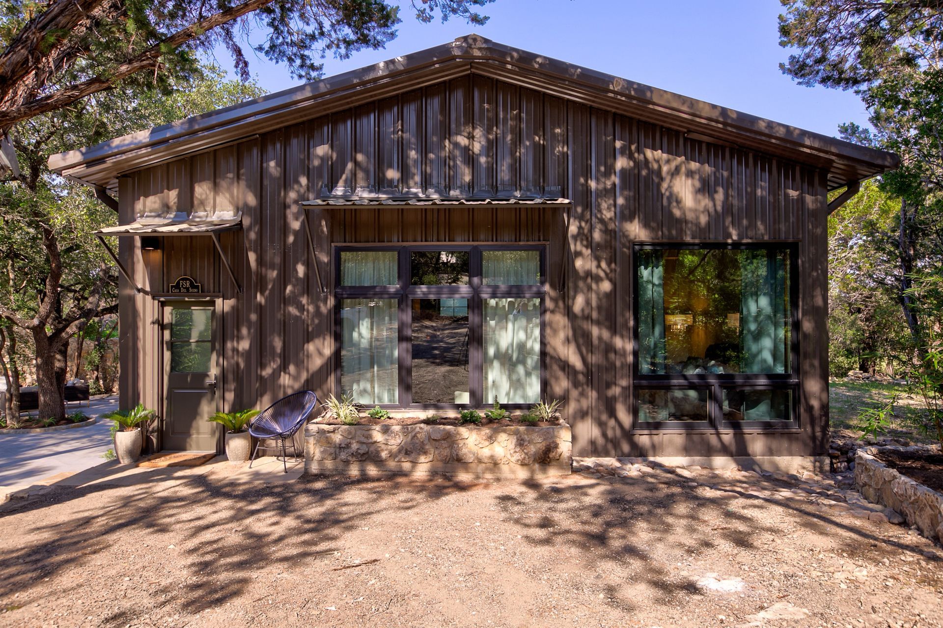 A small house with a lot of windows is surrounded by trees.