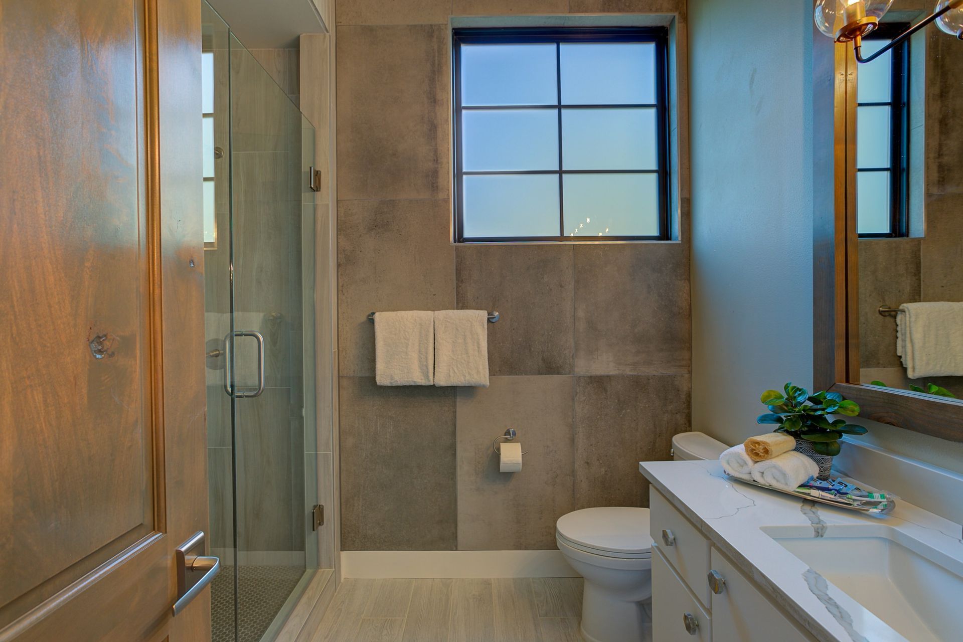 A bathroom with a toilet , sink , shower and window.