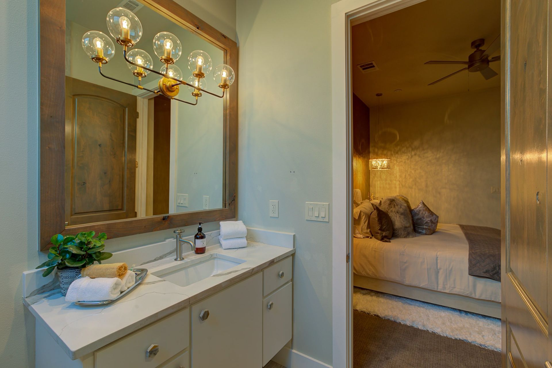 A bathroom with a sink , mirror and ceiling fan leading to a bedroom.