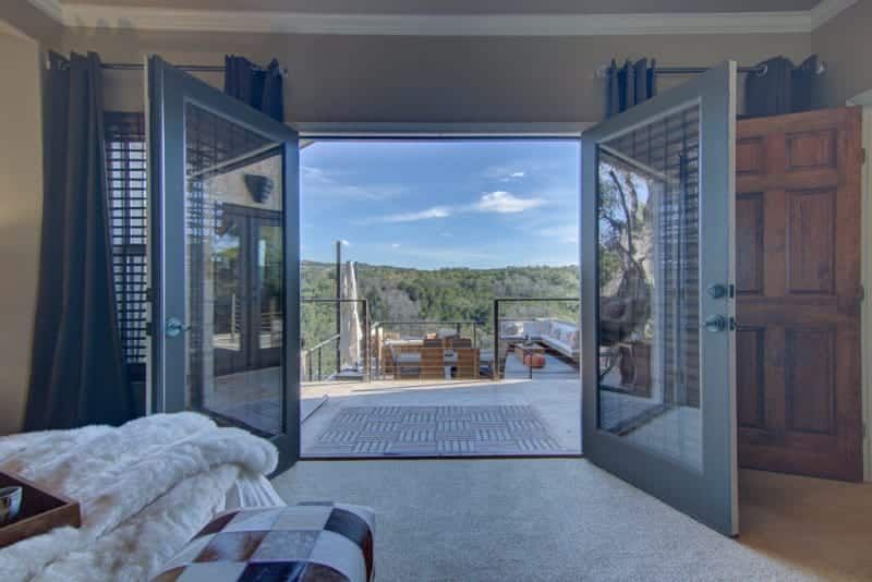 A bedroom with a view of a deck and mountains from the window.
