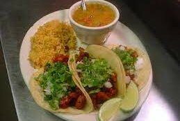 A plate of tacos , rice and a bowl of soup on a table.