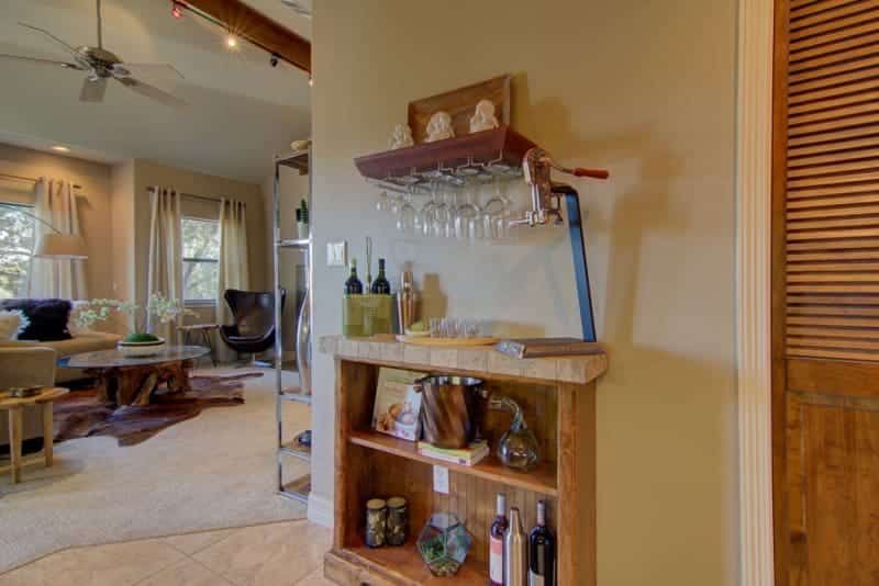 A wooden shelf with wine bottles and glasses on it in a living room.