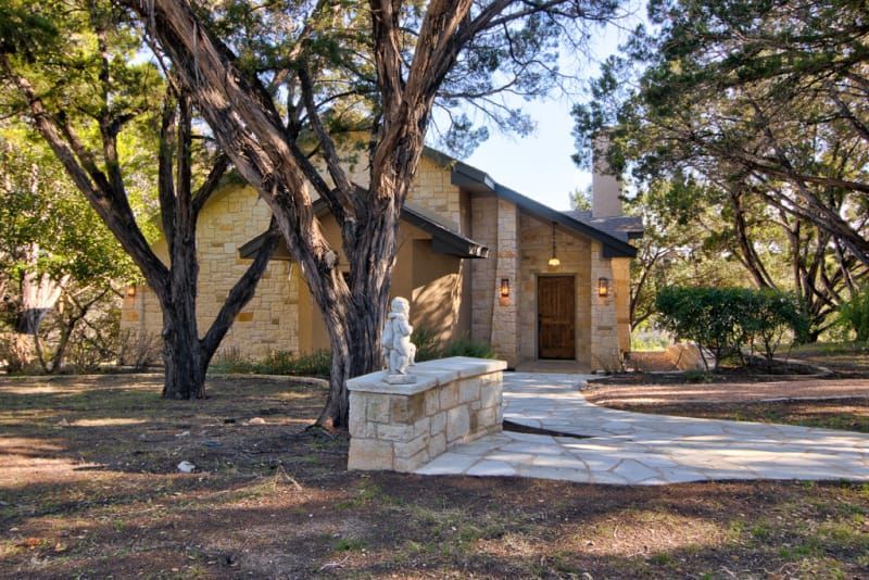 A house with a stone walkway leading to it is surrounded by trees.