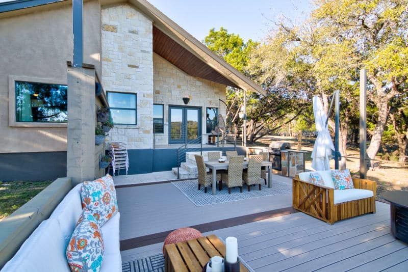 A patio with a couch , chairs , table and umbrellas in front of a house.