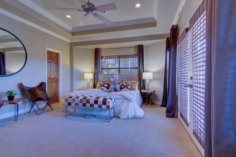 A bedroom with a bed , bench , mirror and ceiling fan.