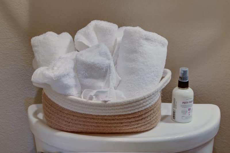 A basket filled with towels and a spray bottle on a toilet.