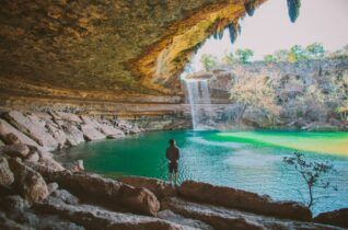 A man is standing in front of a waterfall in a cave.