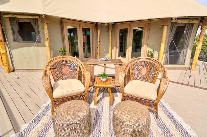 There are two chairs and a table on the deck of a tent.