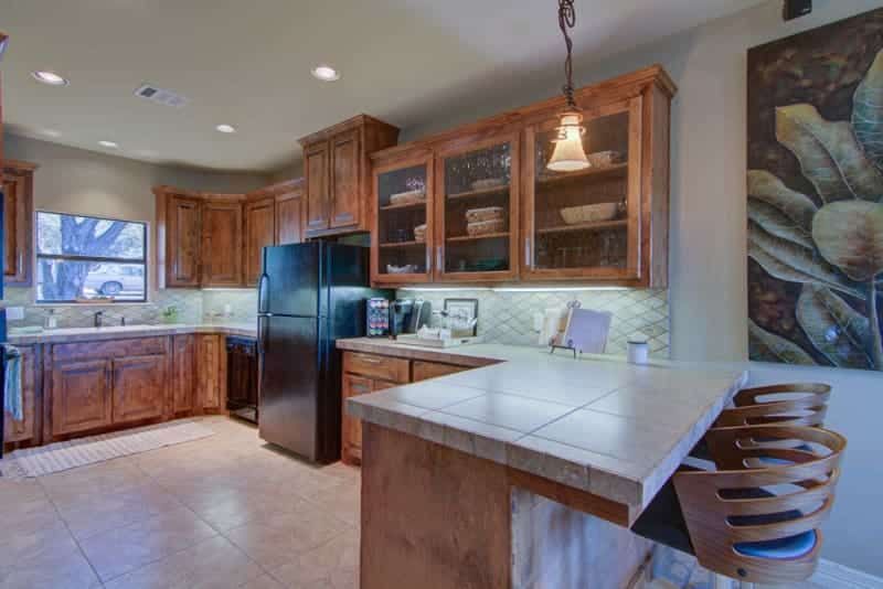 A kitchen with wooden cabinets , a refrigerator , a sink , and a bar.